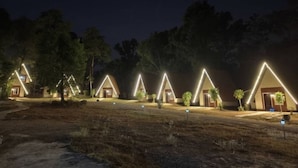 Una hilera de cabañas con techos triangulares y contornos iluminados, rodeadas de árboles y un sendero de tierra.