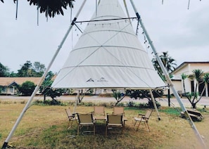 A large white tent with a logo, surrounded by four chairs and a table, set up in an outdoor area with grass and a few trees. - Ku pa Jiao Garden Hotel (Thakhek)