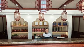 Zona de recepción de un hotel con mostrador de caja, estanterías llenas de botellas de licor y certificados enmarcados.