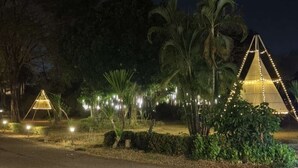 Un espacio exterior nocturno con una estructura parecida a una tienda de campaña, luces colgantes y una pequeña construcción en forma de pirámide.