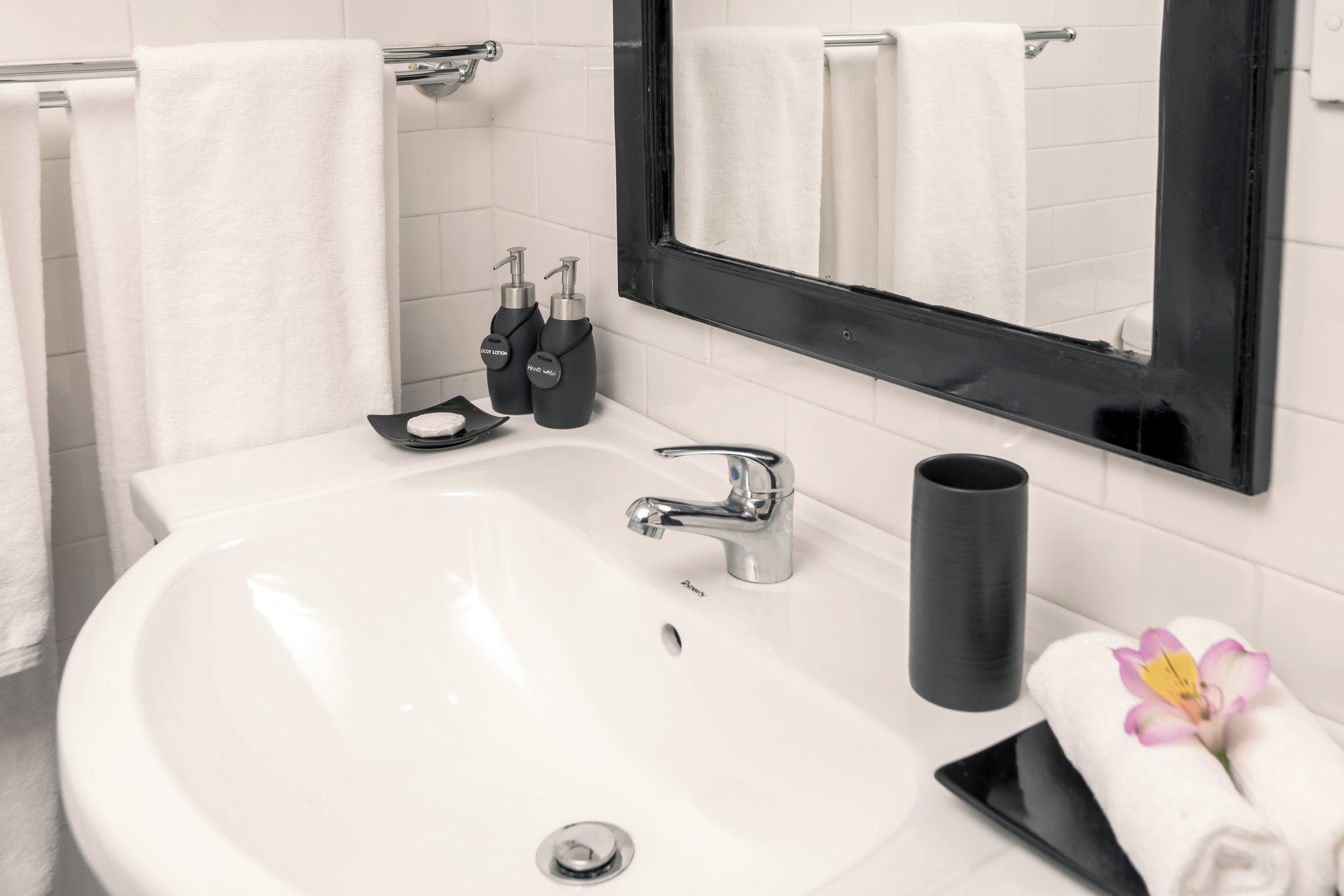 A bathroom with a white sink, a black faucet, two soap dispensers, a black soap dish, and a black cylindrical container.
