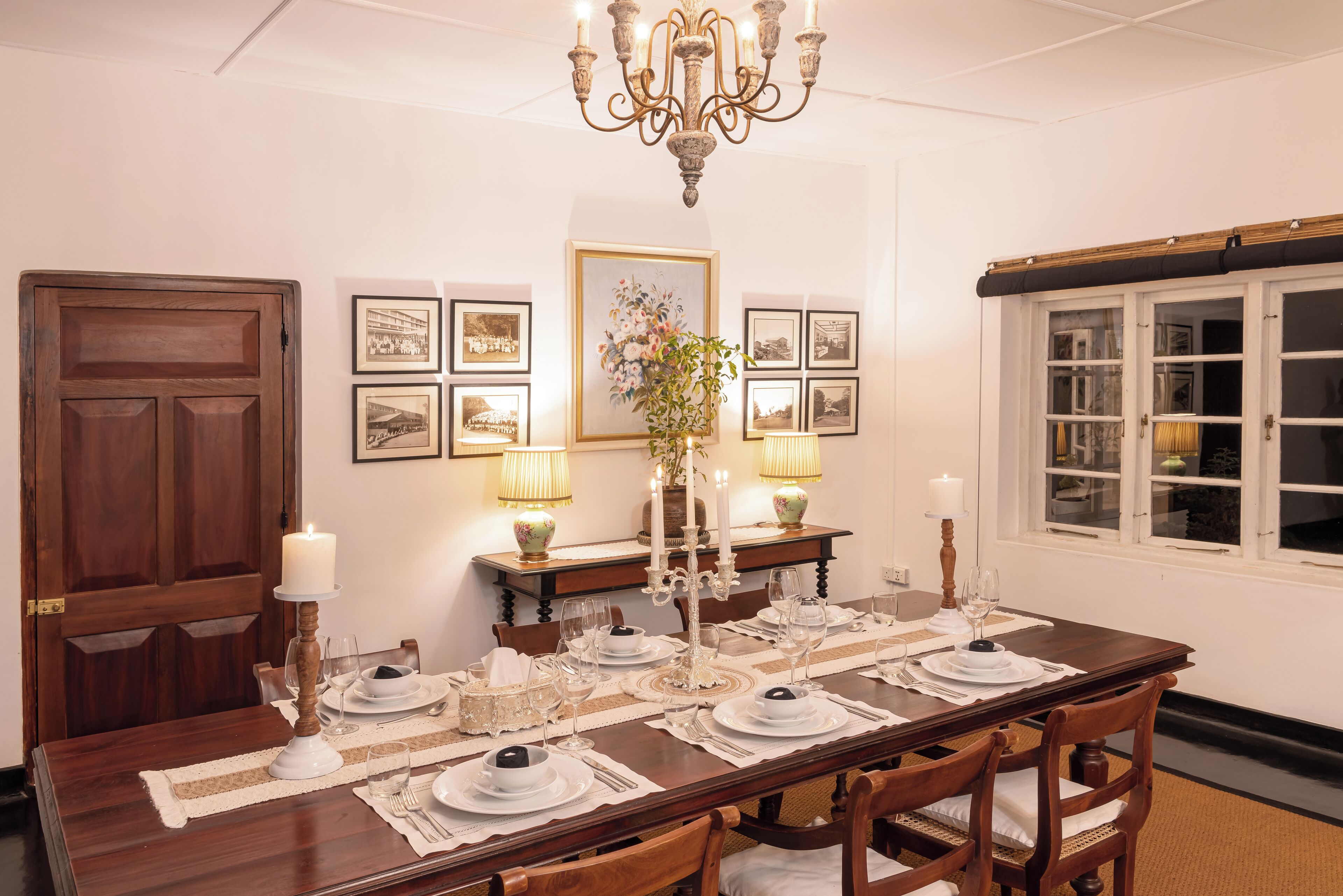 A dining room with a wooden table set for four, surrounded by chairs, a chandelier, and framed pictures on the wall.