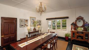 Uma sala de jantar com uma mesa de madeira comprida, cadeiras, um lustre, quadros, uma janela e um espelho.