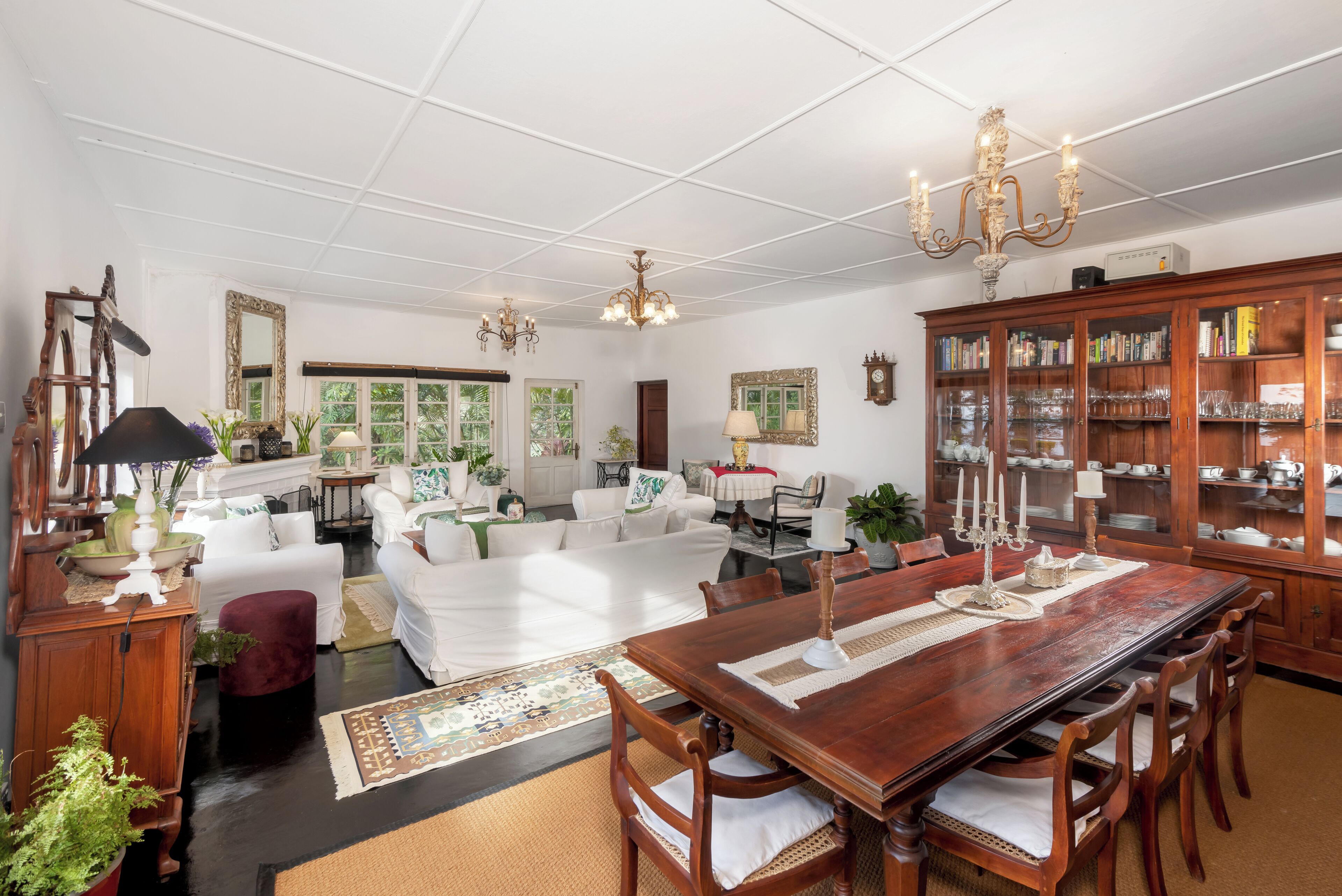 Un salón amplio con una gran mesa de comedor de madera, sofás blancos y una araña.