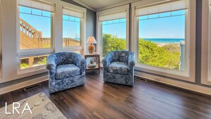 A room with two patterned armchairs, a small table with a lamp, and large windows offering a view of the beach. - The Sandlot - Renovated & Right on the Beach! (Topsail Beach)