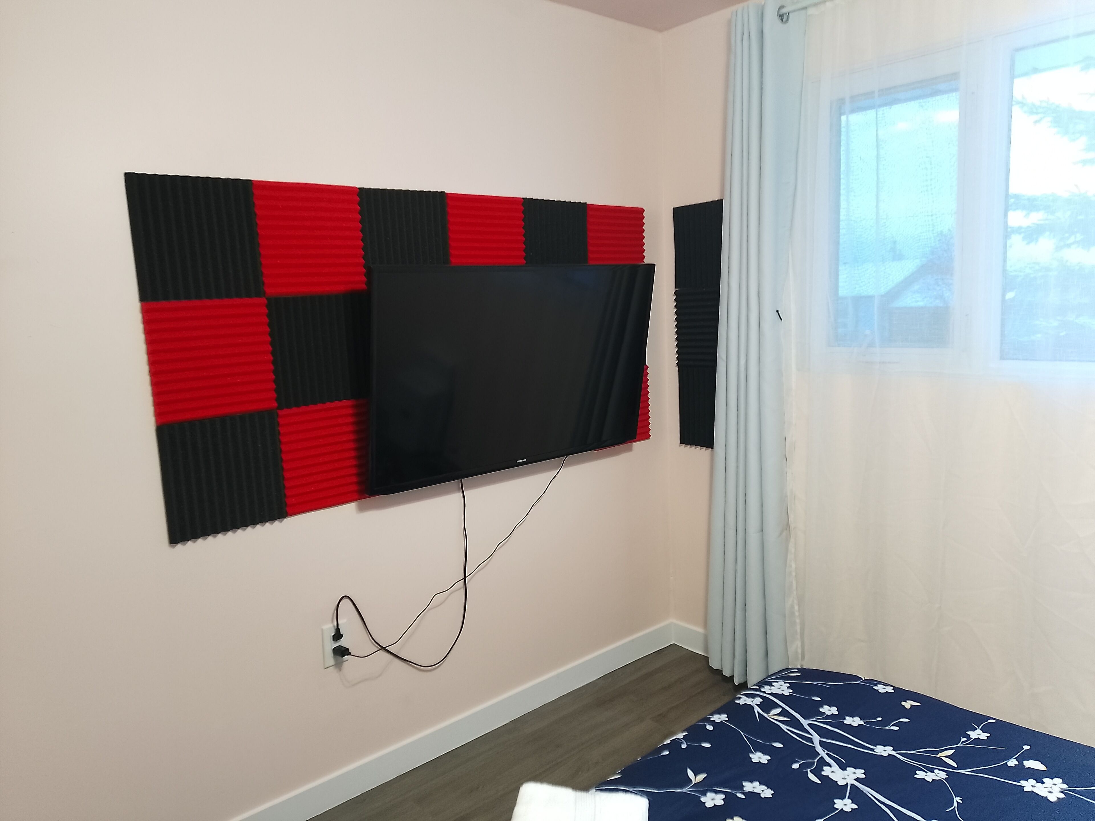 A room with a mounted TV on a wall, a power outlet, and a window with curtains.