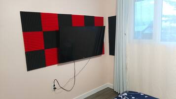 A room with a mounted TV on a wall, a power outlet, and a window with curtains.