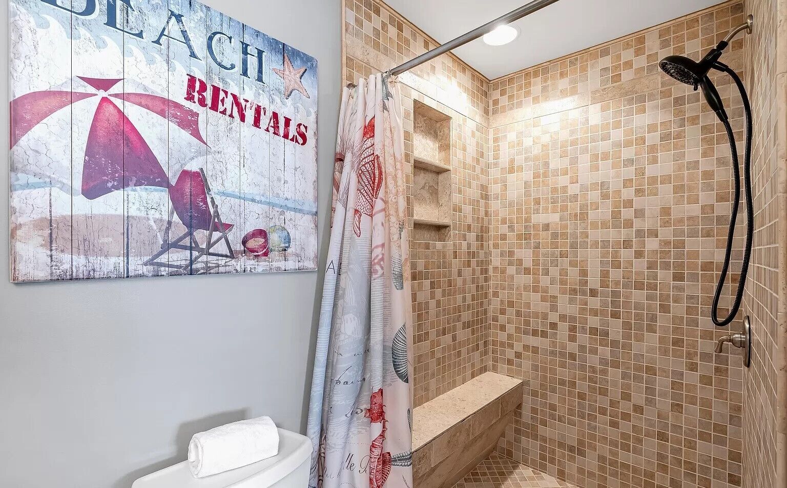 A bathroom with a shower, a towel on the sink, and a beach-themed wall decoration.