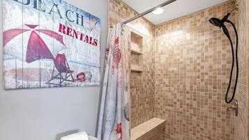 A bathroom with a shower, a towel on the sink, and a beach-themed wall decoration.