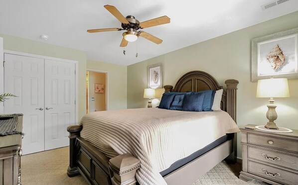 Un dormitorio con cama, mesitas de noche, cómoda, ventilador de techo y puerta.