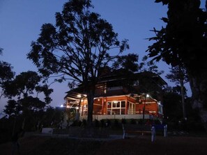A two-story building with a covered outdoor area, surrounded by trees. - I-ROOMZ Donimoole Homestay (Mudigere)