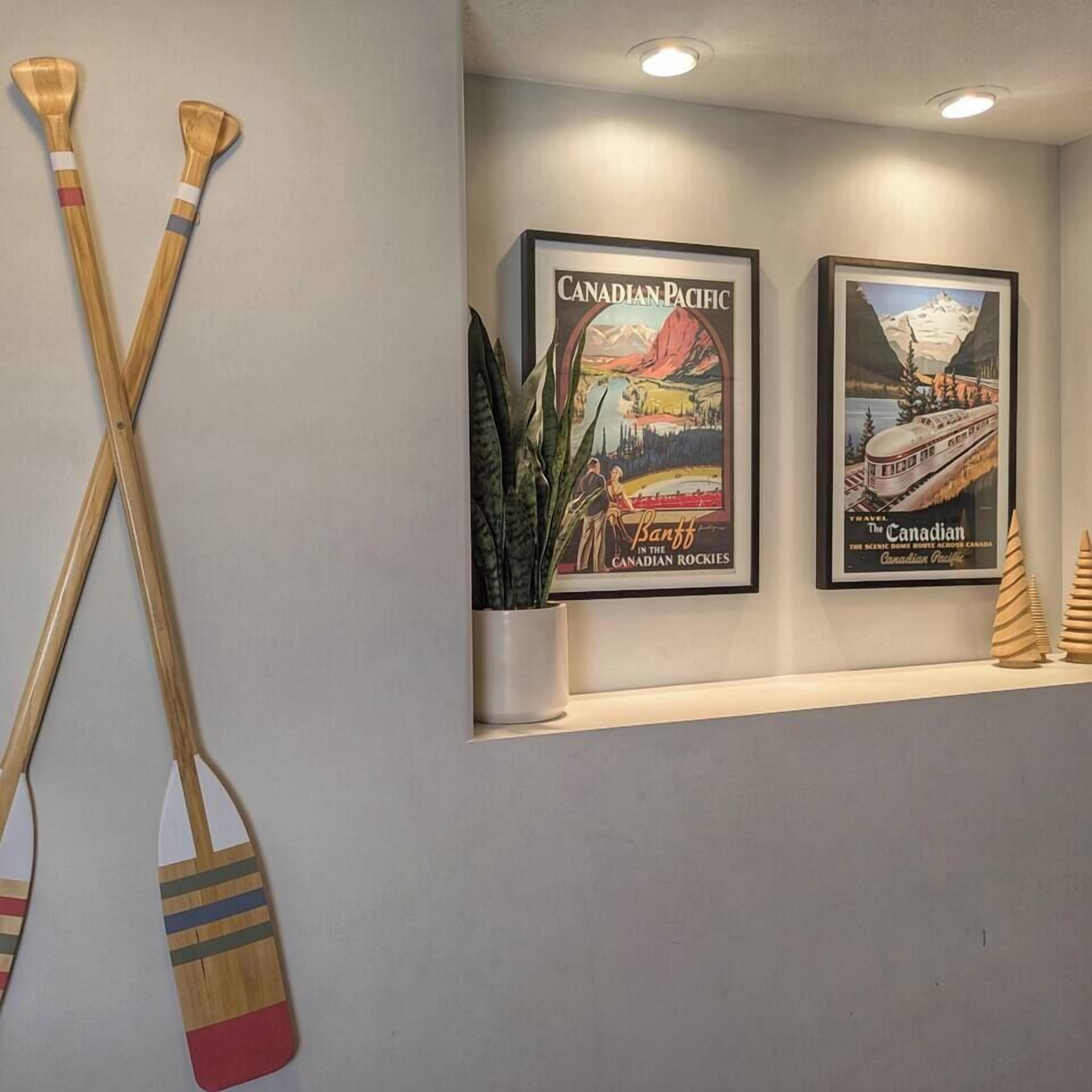 Two framed travel posters of the Canadian Pacific Railway and a pair of wooden paddles on a wall.
