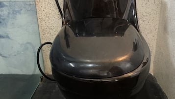 A black toilet with a visible water pipe and a wall with a speckled pattern.