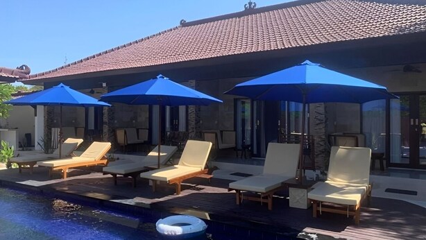 A poolside area with lounge chairs and blue umbrellas. - Relax Villas Gili Air (Gili Air)