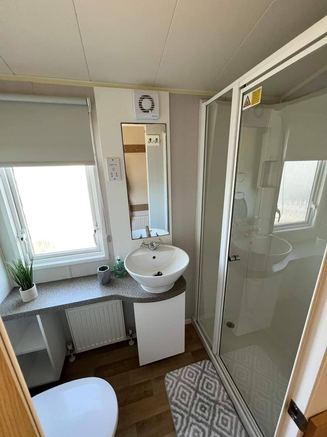 Un baño de autocaravana pequeño con lavabo, espejo y ducha.