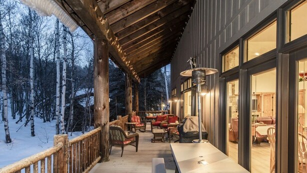Een houten terras met buitenmeubels, een tafel en een barbecue, met uitzicht op een besneeuwd bos.