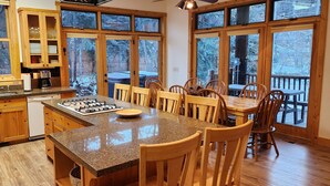 Een keuken met houten kastjes, een granieten aanrecht en een groot kookeiland met stoelen. Grote ramen bieden uitzicht op een besneeuwde achtertuin.
