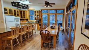 Een ruime keuken met houten kastjes, een eethoek met stoelen en grote ramen met uitzicht op het landschap.