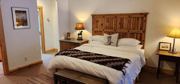 A bedroom with a wooden headboard, a bed with white linens, a patterned throw blanket, a nightstand with a lamp, and a framed picture on the wall. - Sundance, Spacious Vaulted Ceiling Cabin, Hot Tub, Huge Lawn, Mountain Views. (Sundance)