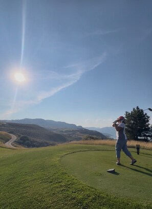 En golfbana med klar himmel, en golfspelare mitt i svingen och ett bergskedja i fjärran.