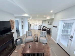 Een moderne woonkamer met een flatscreen televisie, een open haard, en een eethoek met twee stoelen en een tafel.