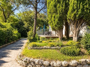 Un jardin avec un chemin en pierre, un espace aménagé avec des tables et des chaises, ainsi que divers arbres et arbustes.