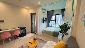A modern hotel room with a bed, a sofa, a small table, and a dining area with chairs. - SURIHOME- Vinhomes Grand Park Apartments (Ho Chi Minh City)