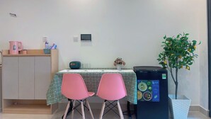 A small dining area with a table, two pink chairs, a cabinet, a water dispenser, and a potted plant. - SURIHOME- Vinhomes Grand Park Apartments (Ho Chi Minh City)
