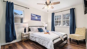 Een slaapkamer met een bed, nachtkastjes, een stoel, een plafondventilator en een raam met gordijnen.