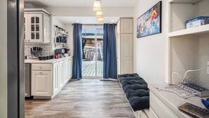 Een smalle gang met een keuken aan de ene kant, een bank met een stekkerdoos, en een deur naar een buitenruimte.