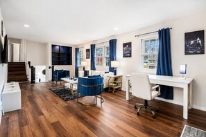 A modern hotel room with a wooden floor, a desk, a chair, a sofa, and a staircase.