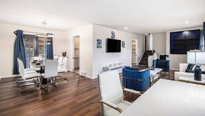 Een moderne woonkamer met een eethoek, een trap en een aan de muur bevestigde televisie.