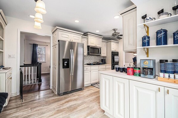 A modern kitchen with white cabinetry, stainless steel appliances, and a central island. - A Touch of Luxury - Arcade, 5 TVs, Bounce House, Coffee Bar (Omaha)