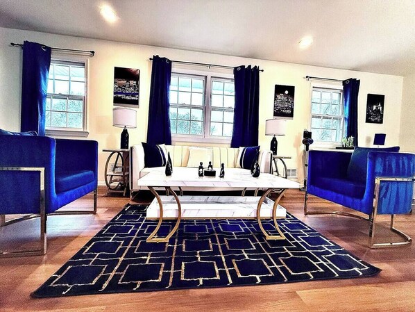 A room with a white sofa, a blue sofa, a coffee table, and a patterned rug. - A Touch of Luxury - Arcade, 5 TVs, Bounce House, Coffee Bar (Omaha)