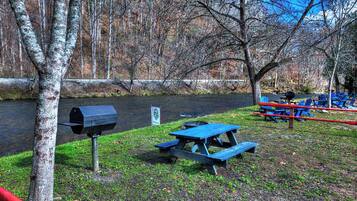 A picnic area with a grill and benches by a river.