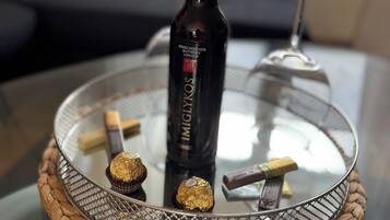 A glass table with a woven base, a bottle of wine, and chocolates.