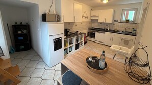 Een kleine keuken met witte kastjes, een inbouwoven en een magnetron. Er staat een houten tafel met een dienblad en een fles.