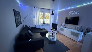 Een moderne woonkamer met een hoekbank, een glazen salontafel, een televisie en led-verlichting.
