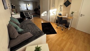 Een moderne, goed verlichte kamer met een bed, een bureau en een stoel. Er is een raam met gordijnen, een plant en een decoratie aan de muur.