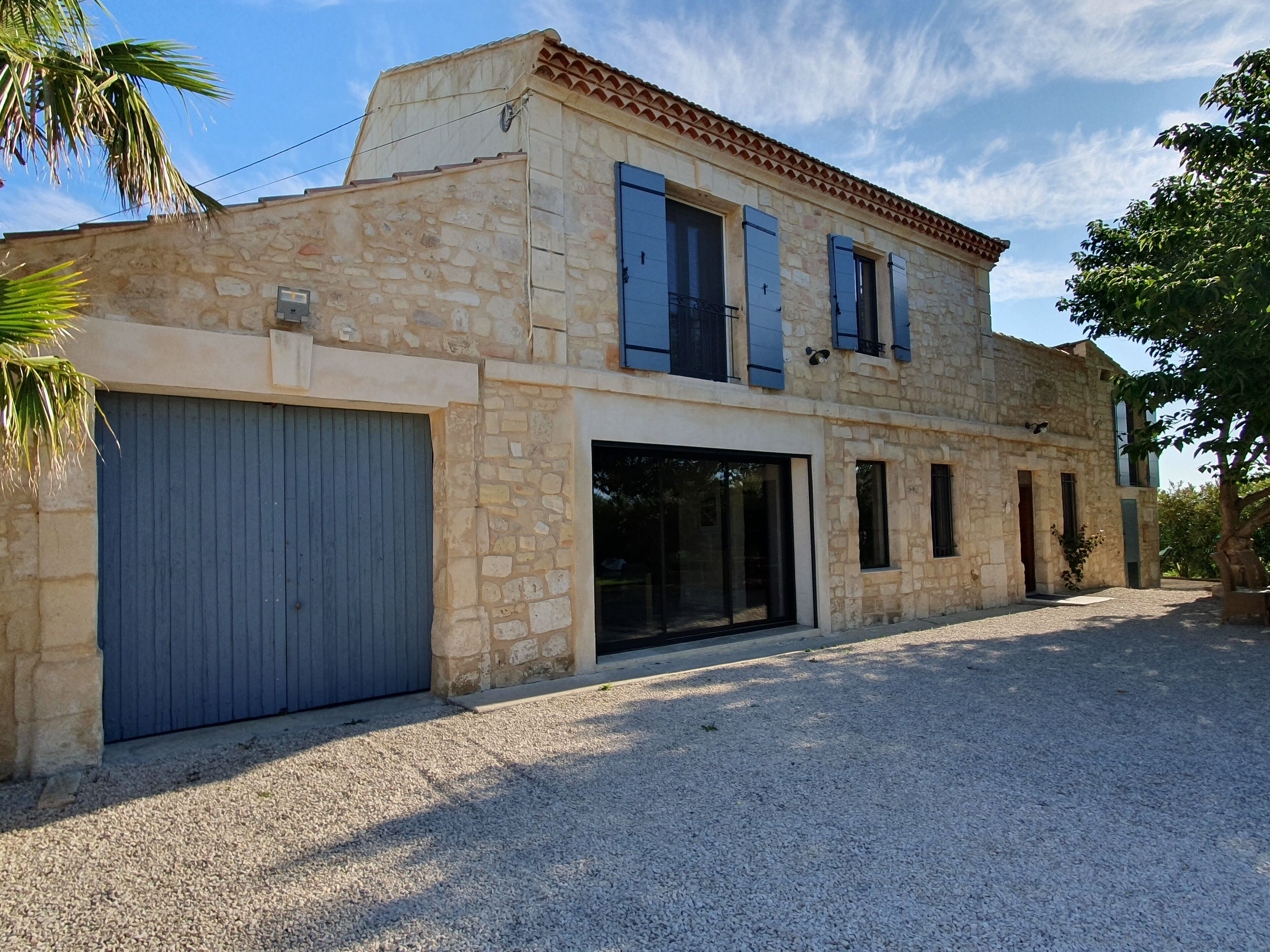 A two-story stone building with a garage, large windows, and a tiled roof.