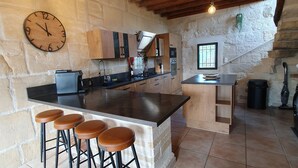 A kitchen with a large island, bar stools, a clock, and stone walls. - CalypSo Luxury Mas Madeleine in Provence (Arles)