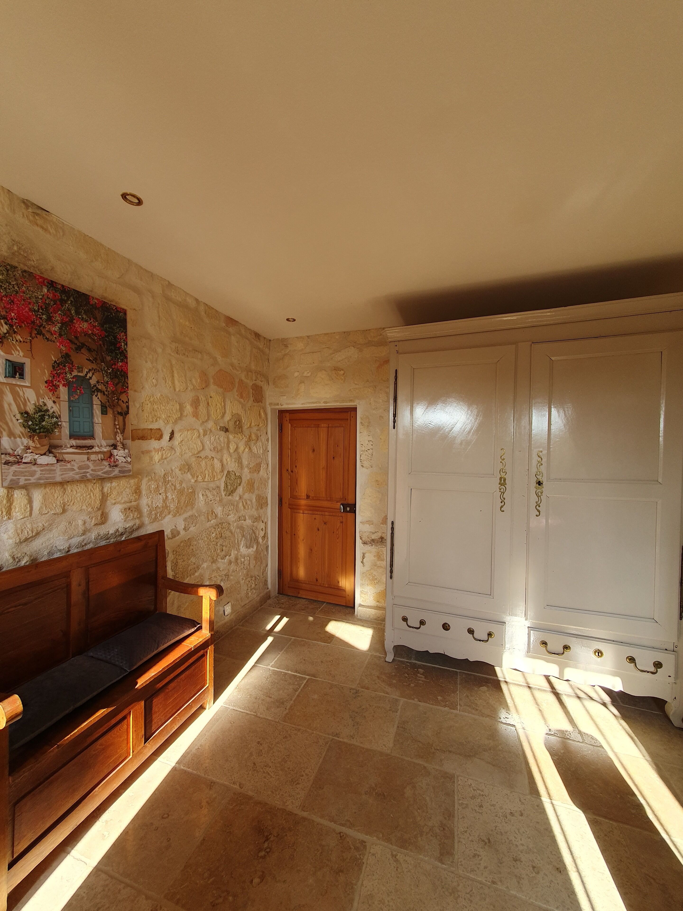 Une pièce avec un mur en pierre, une porte en bois, une armoire blanche et un banc.