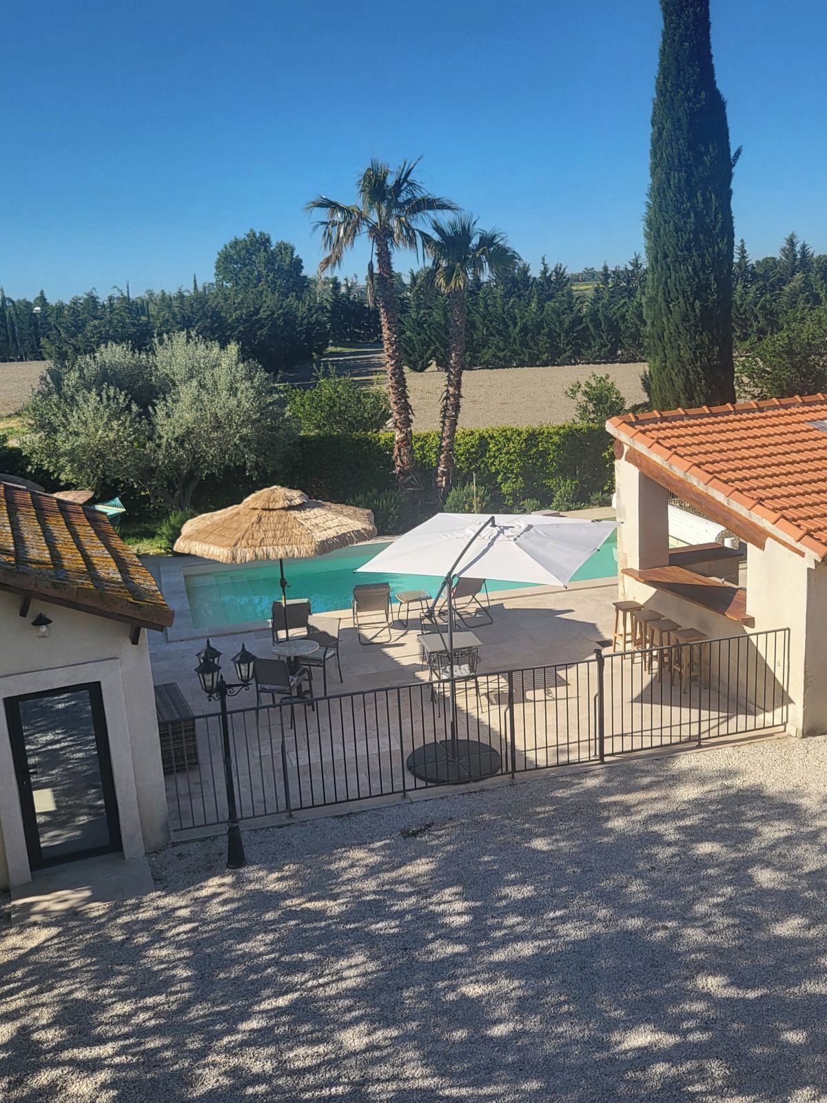 Área da piscina com guarda-sol de palha, assentos externos e vista da paisagem ao redor.