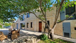 A stone building with a tree in front, outdoor seating, and a car parked nearby. - CalypSo Luxury Mas Madeleine in Provence (Arles)