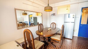A dining area with a round wooden table, six wooden chairs, a mirror, a hanging light fixture, and a refrigerator. - Monratino The Snow roost (Darjeeling)