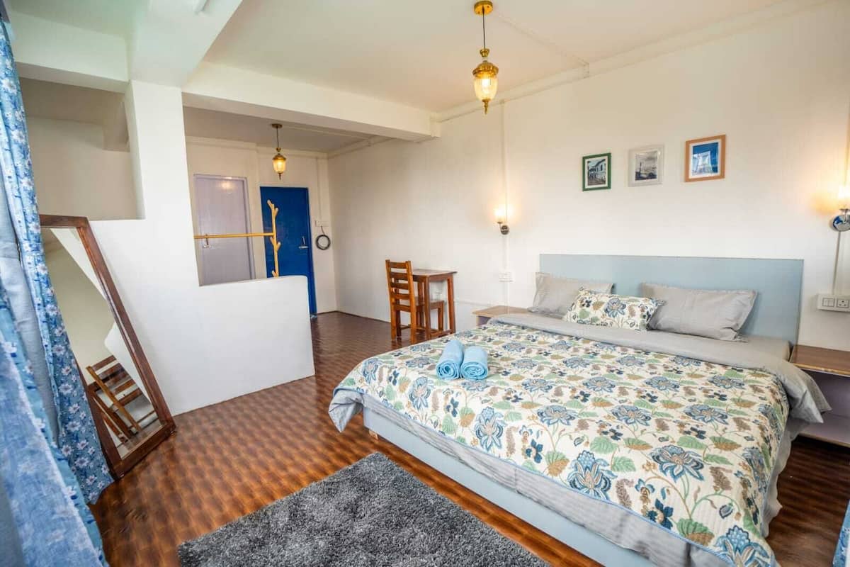 A bedroom with a bed, a desk, and a chair. There is a blue door and a window with curtains.