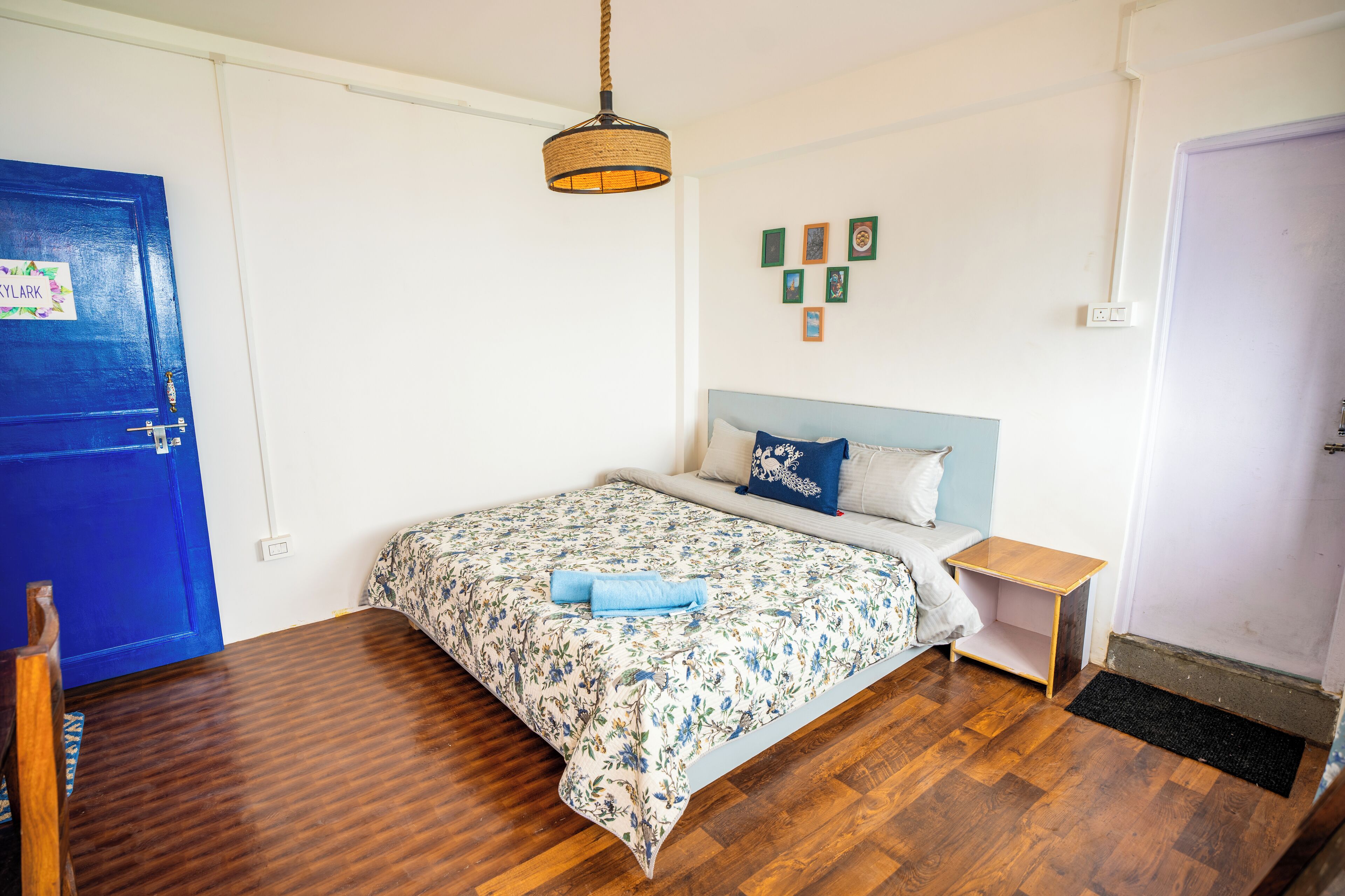 A bedroom with a bed, a nightstand, a blue door, and a hanging light fixture.