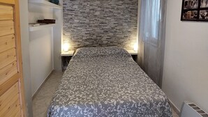 Ein Schlafzimmer mit einem Bett, einer Steinsäule, einem Fenster mit Vorhängen und einem aufgehängten Bild.