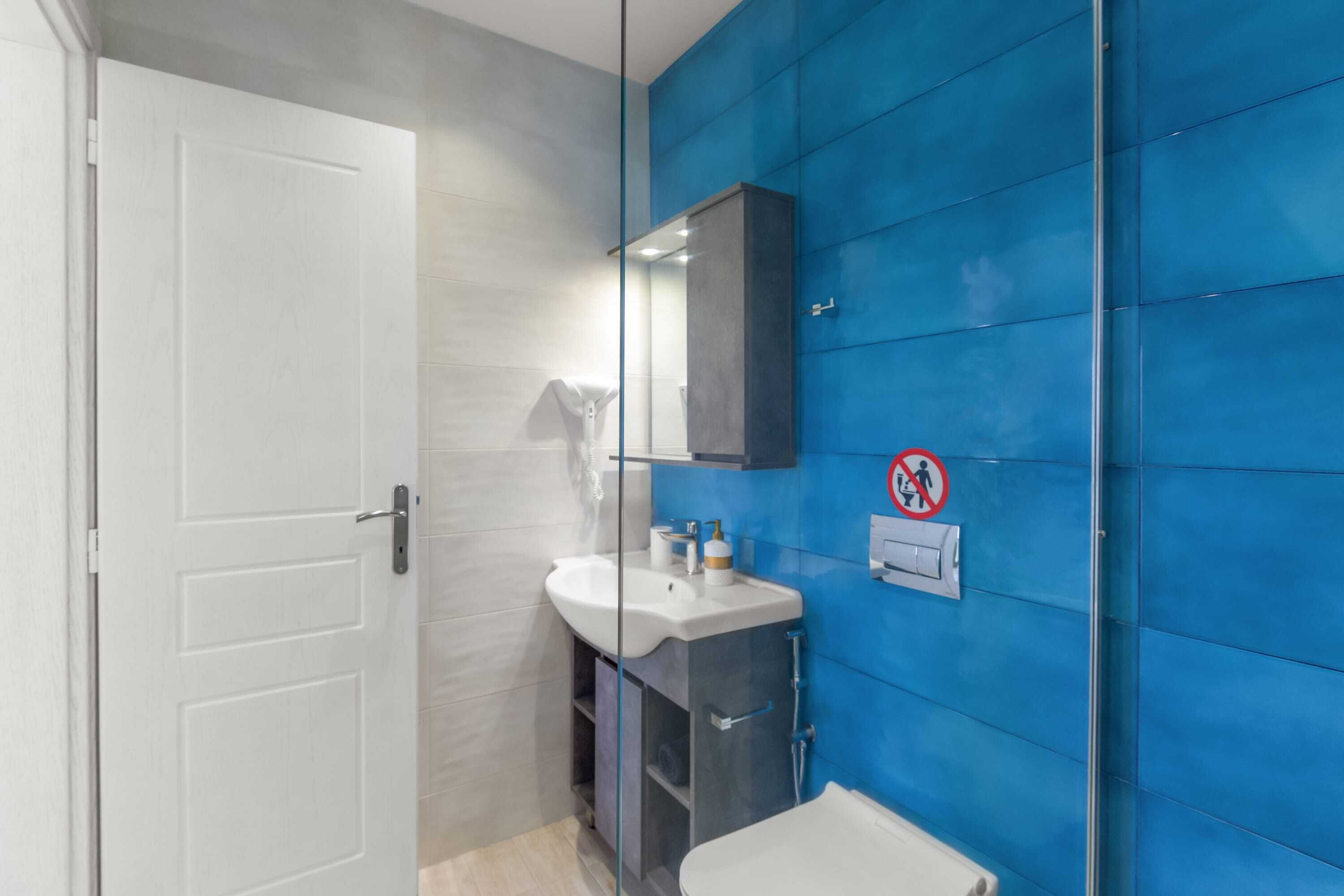 A bathroom with a white door, a sink with a mirror above it, and a blue wall.