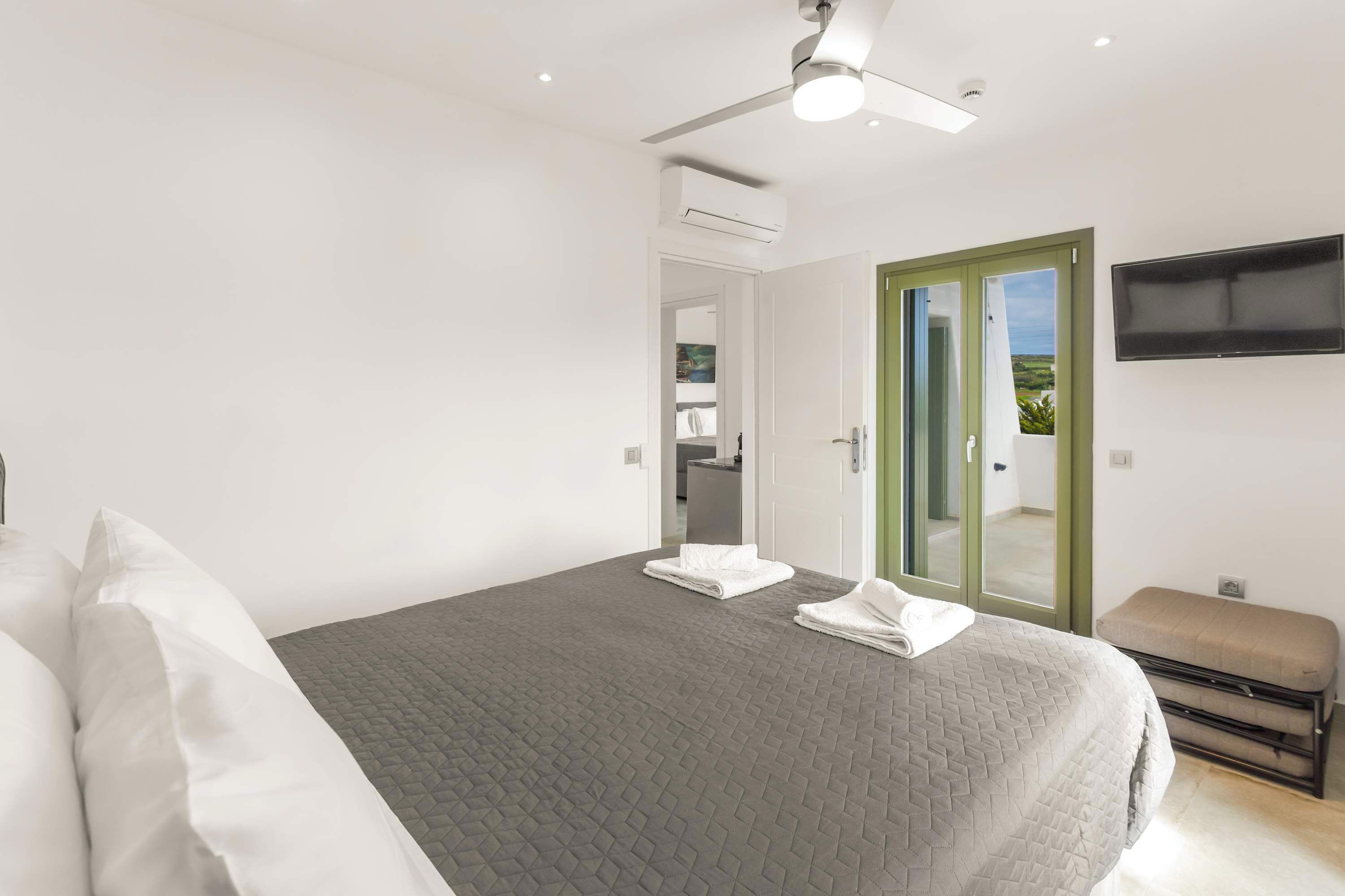 A bedroom with a bed, a bench, a TV, and a door leading to a balcony.